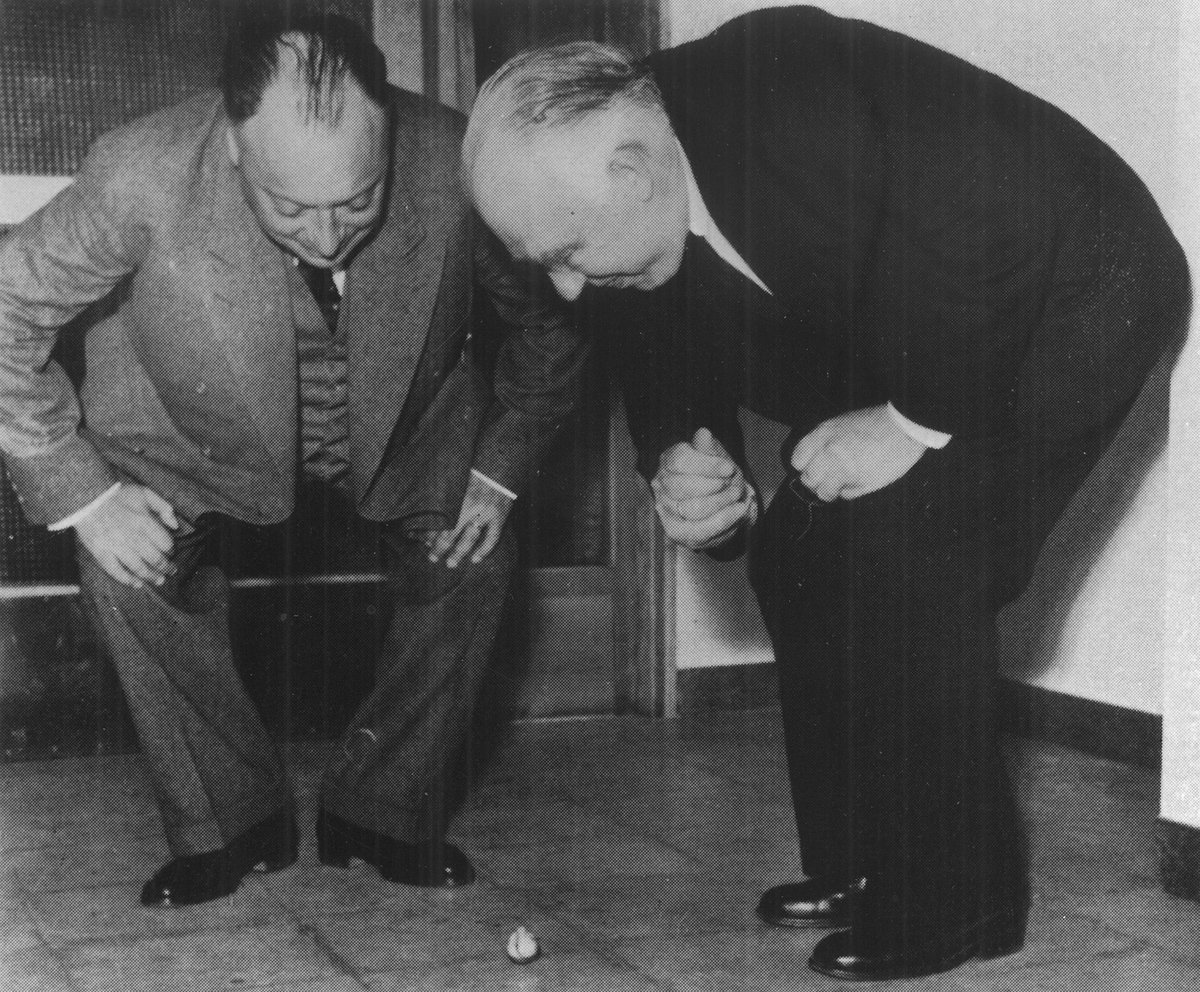 Wolfgang Pauli og Niels Bohr bøjer sig over en tippetop på gulvet
